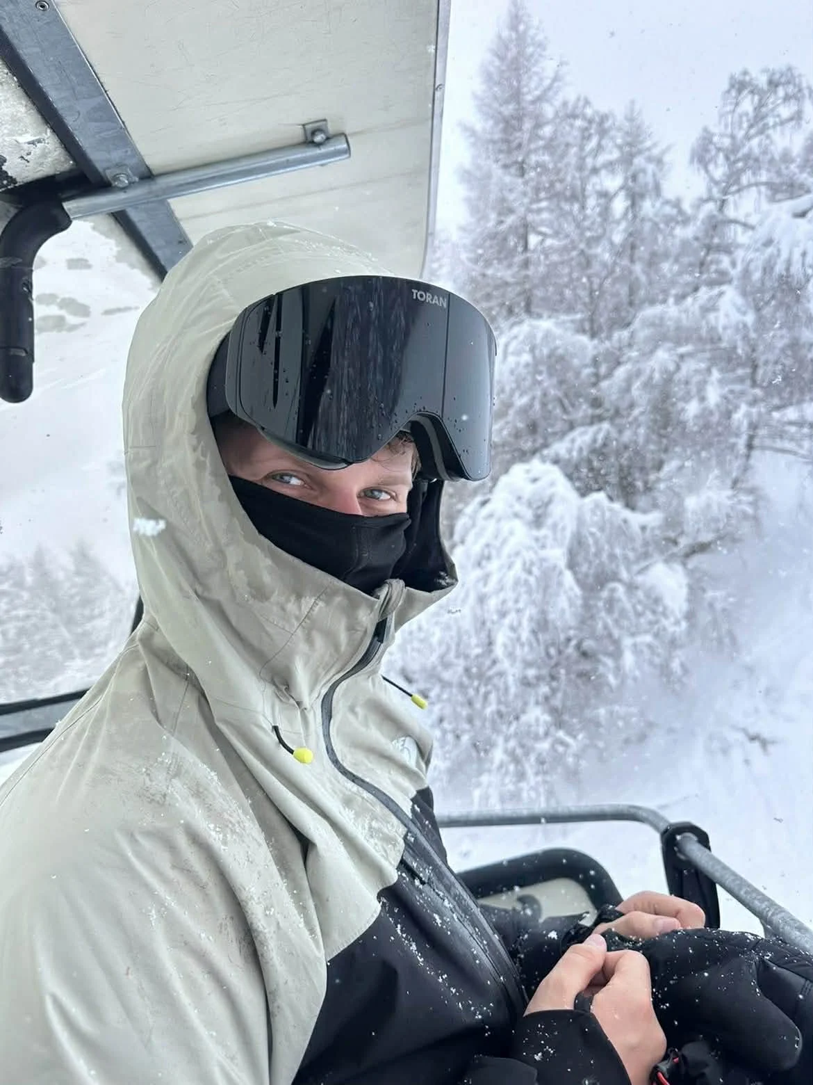 Nærbillede af skiløber med sort TORAN skibrille og halsedisse i stoleliften i snevejr