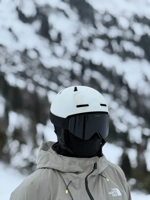 Skiløber med hvid hjelm og TORAN skibrille foran sneklædte træer
