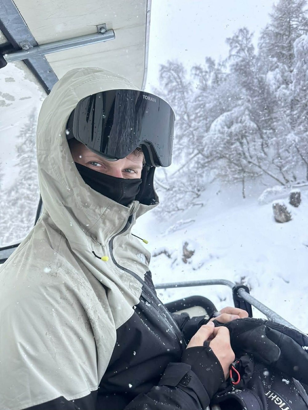 Skiløber med hætte og sort TORAN skibrille i stoleliften med sne på træerne