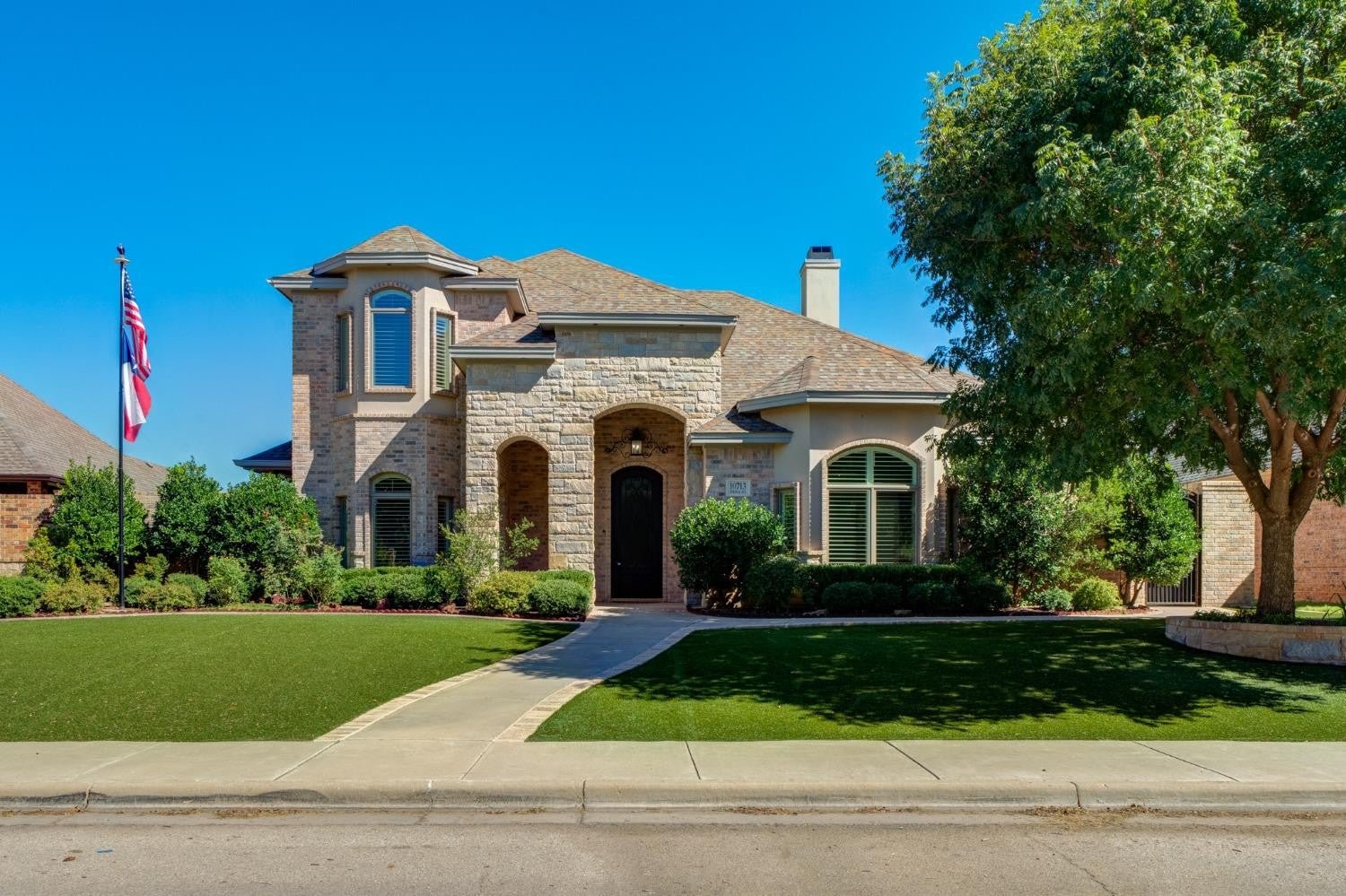 Two-story stone and brick home with mature landscaping and a front walkway.