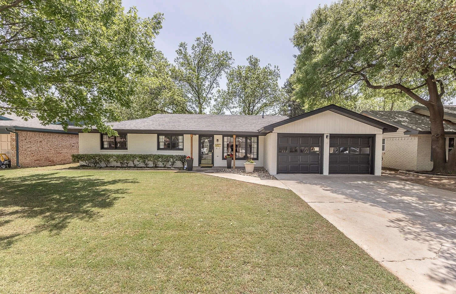Light-painted brick home with dark garage doors and mature shade trees.