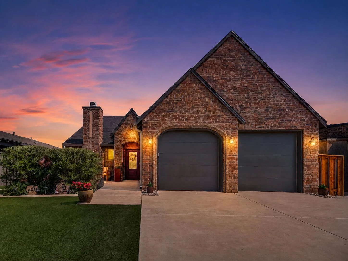 Brick home at sunset with warm exterior lighting and two garage doors.