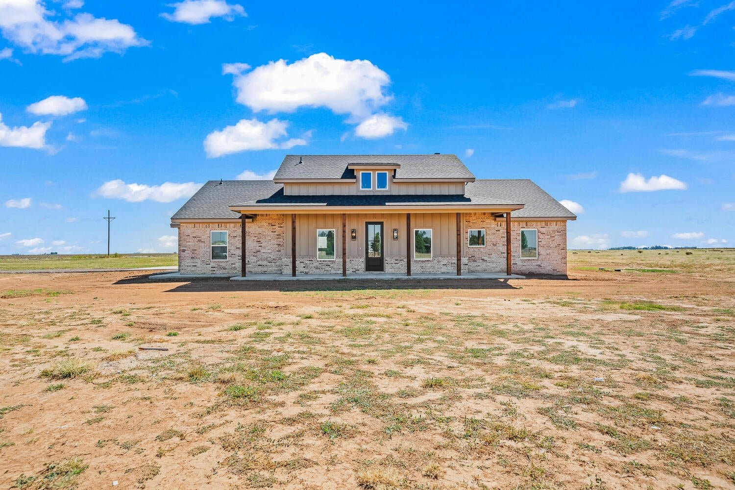 Brick home with a broad covered front porch on an open rural lot.