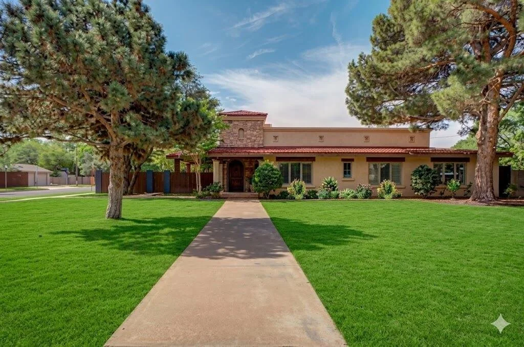 Stucco and stone home framed by mature trees and a green front lawn.