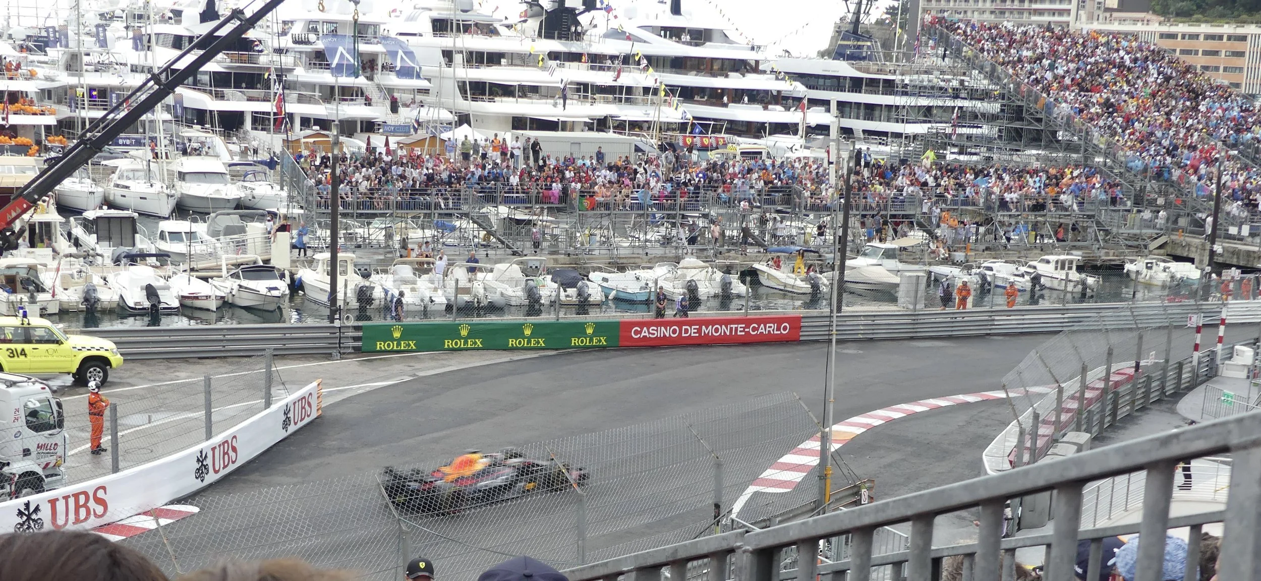 Race cars flying past the harbor, yachts lined up behind the barriers.