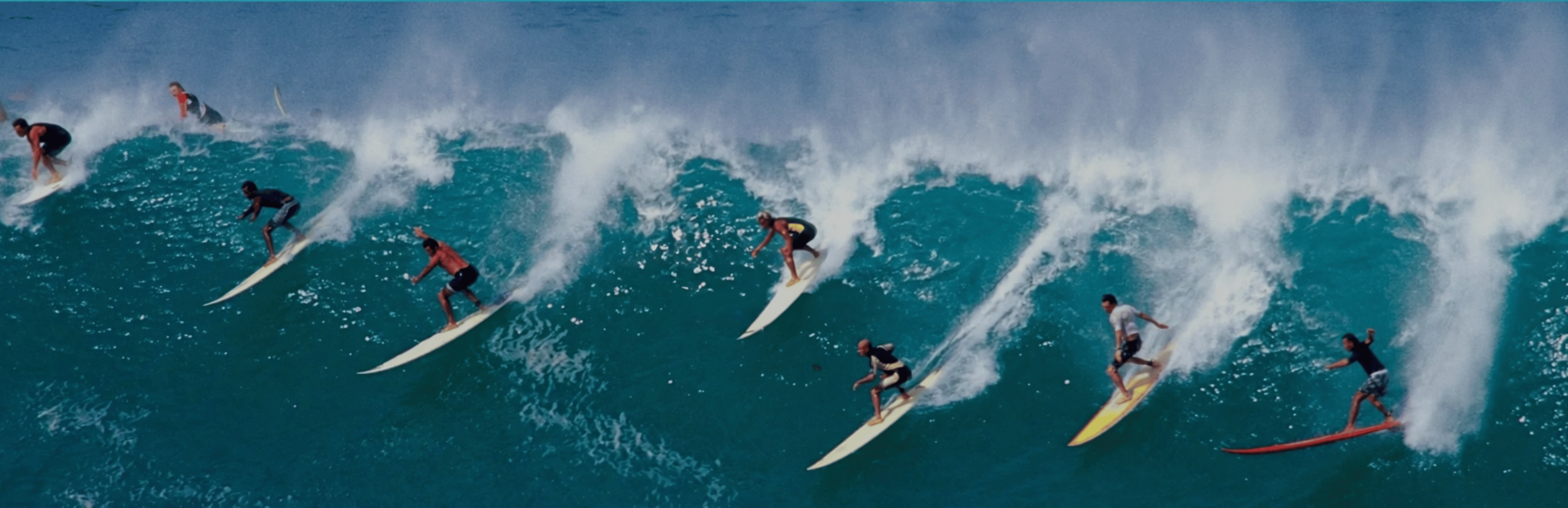 A line of surfers dropping into a powerful ocean wave