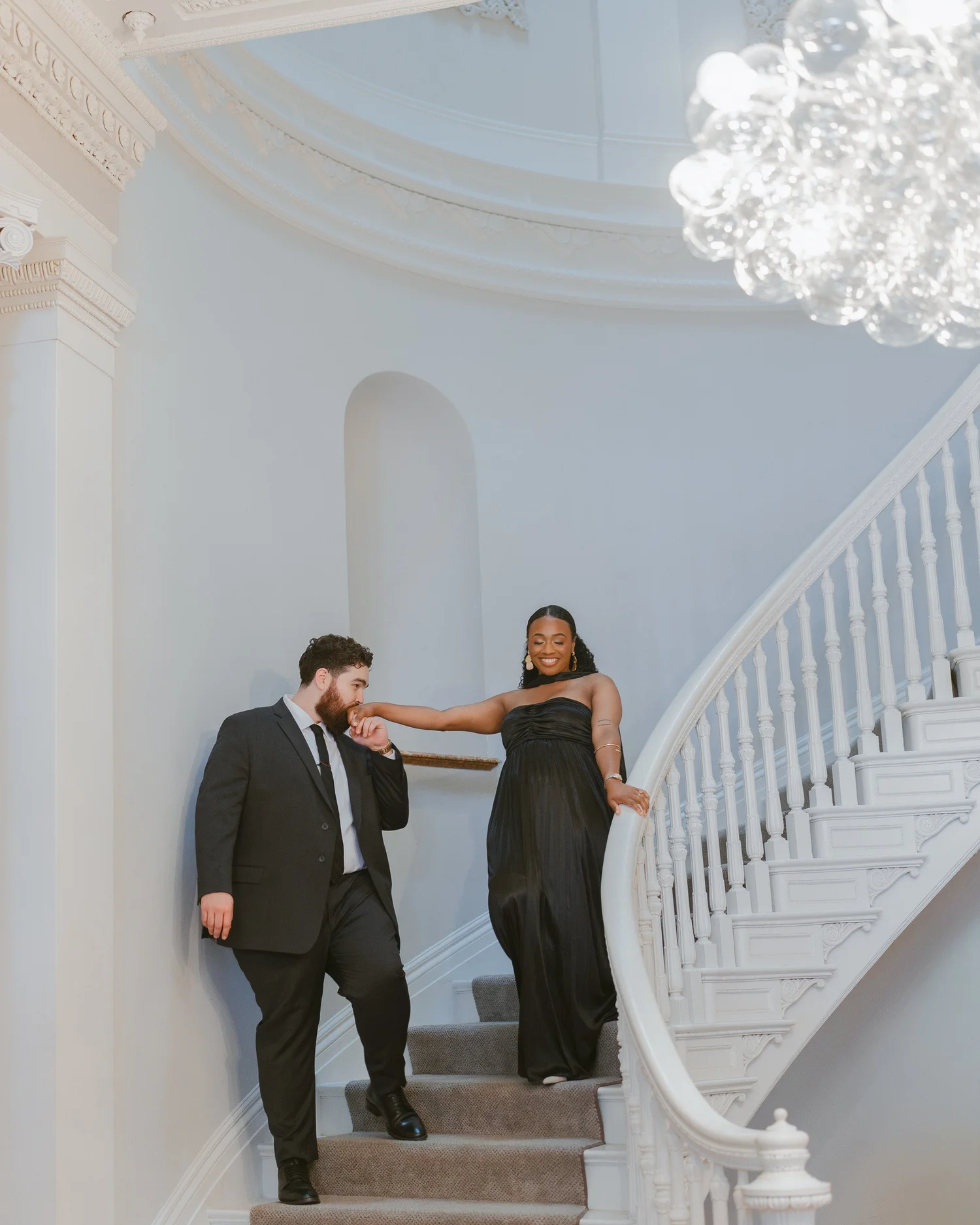 A man kissing his partner's hand on a curved white staircase.