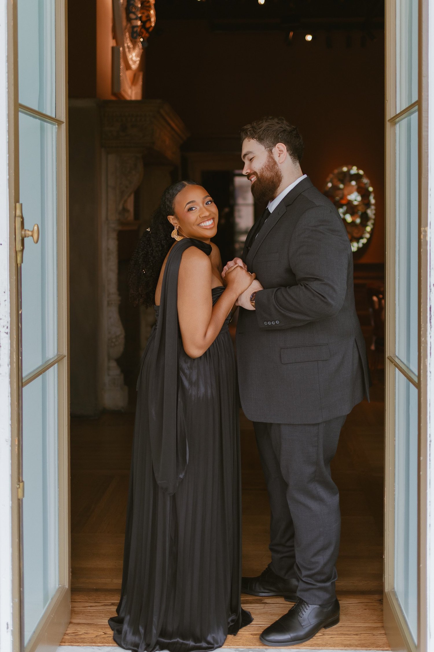 A woman smiling toward the camera while holding her partner in a doorway.