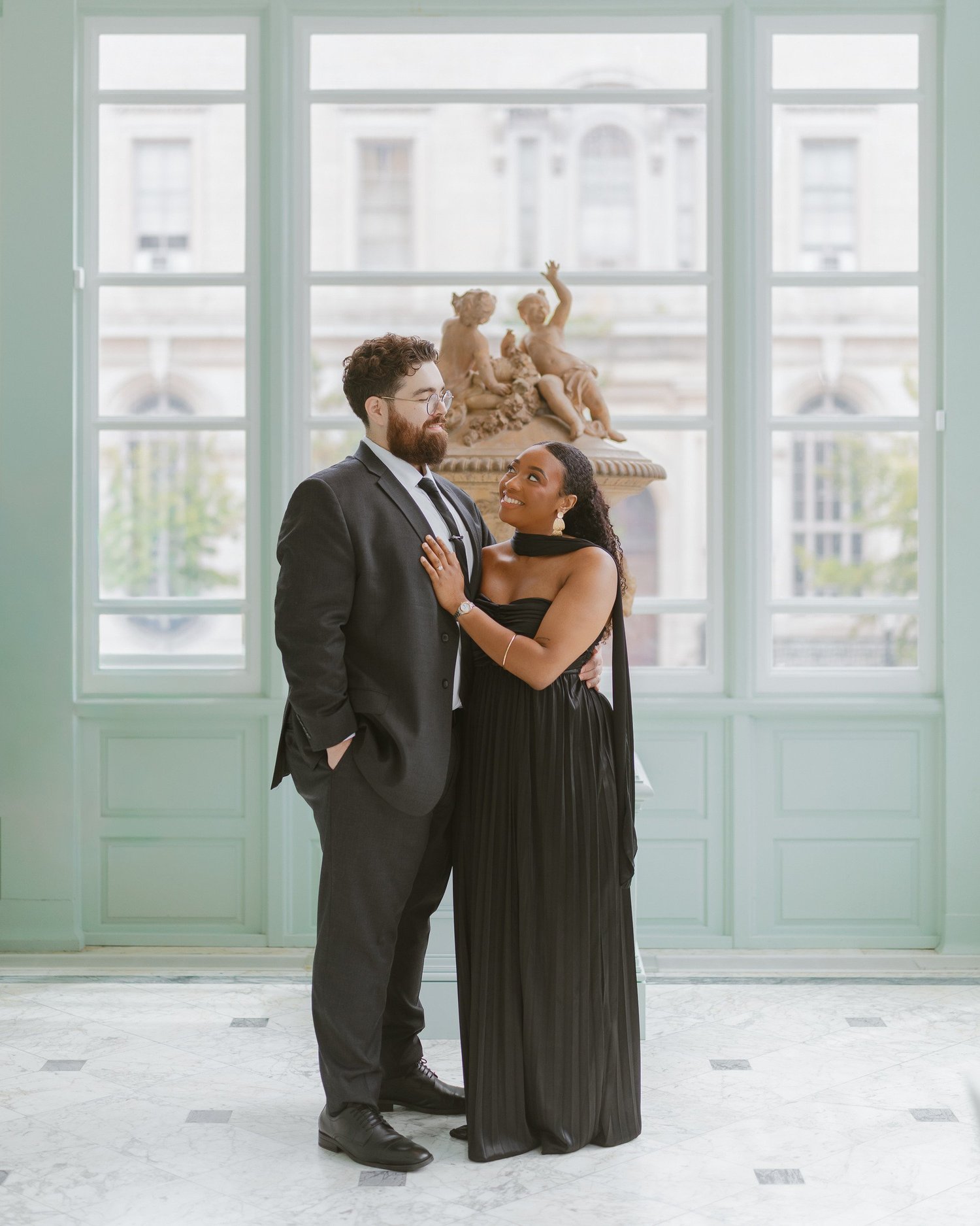 Couple looking at each other in front of tall mint-colored windows.