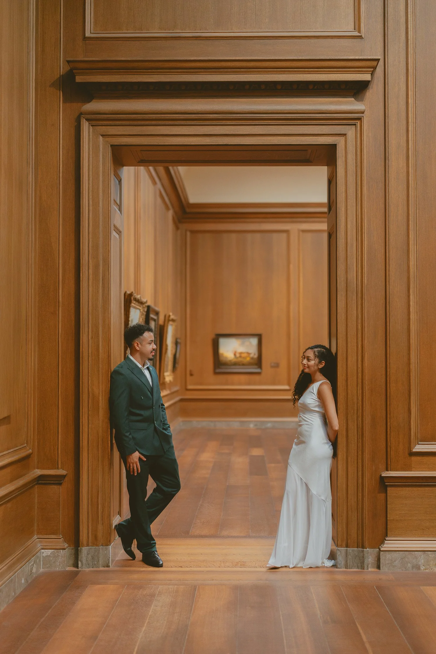 Couple standing at opposite sides of a warm wooden gallery doorway.