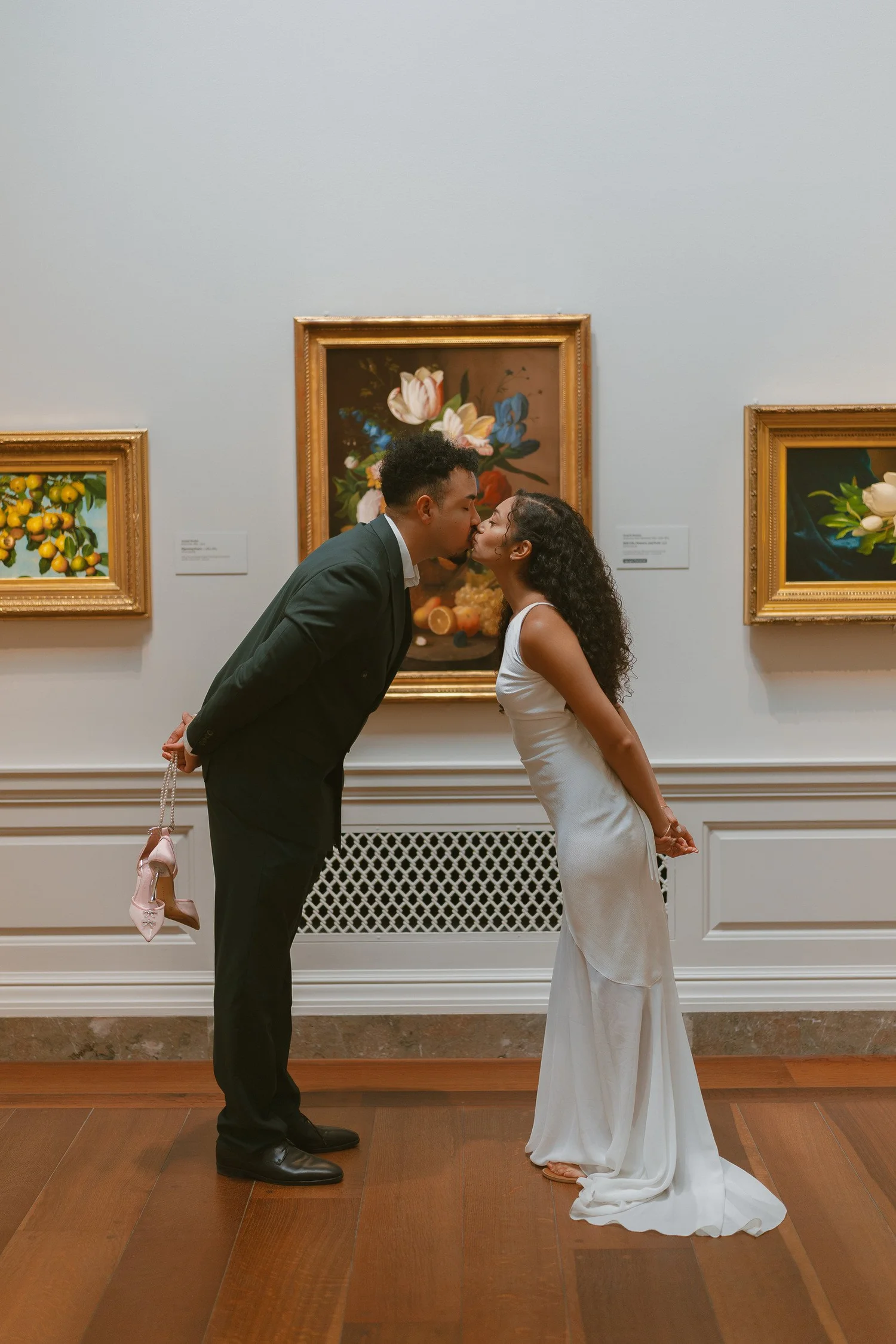 Couple leaning into a kiss in front of framed floral paintings.