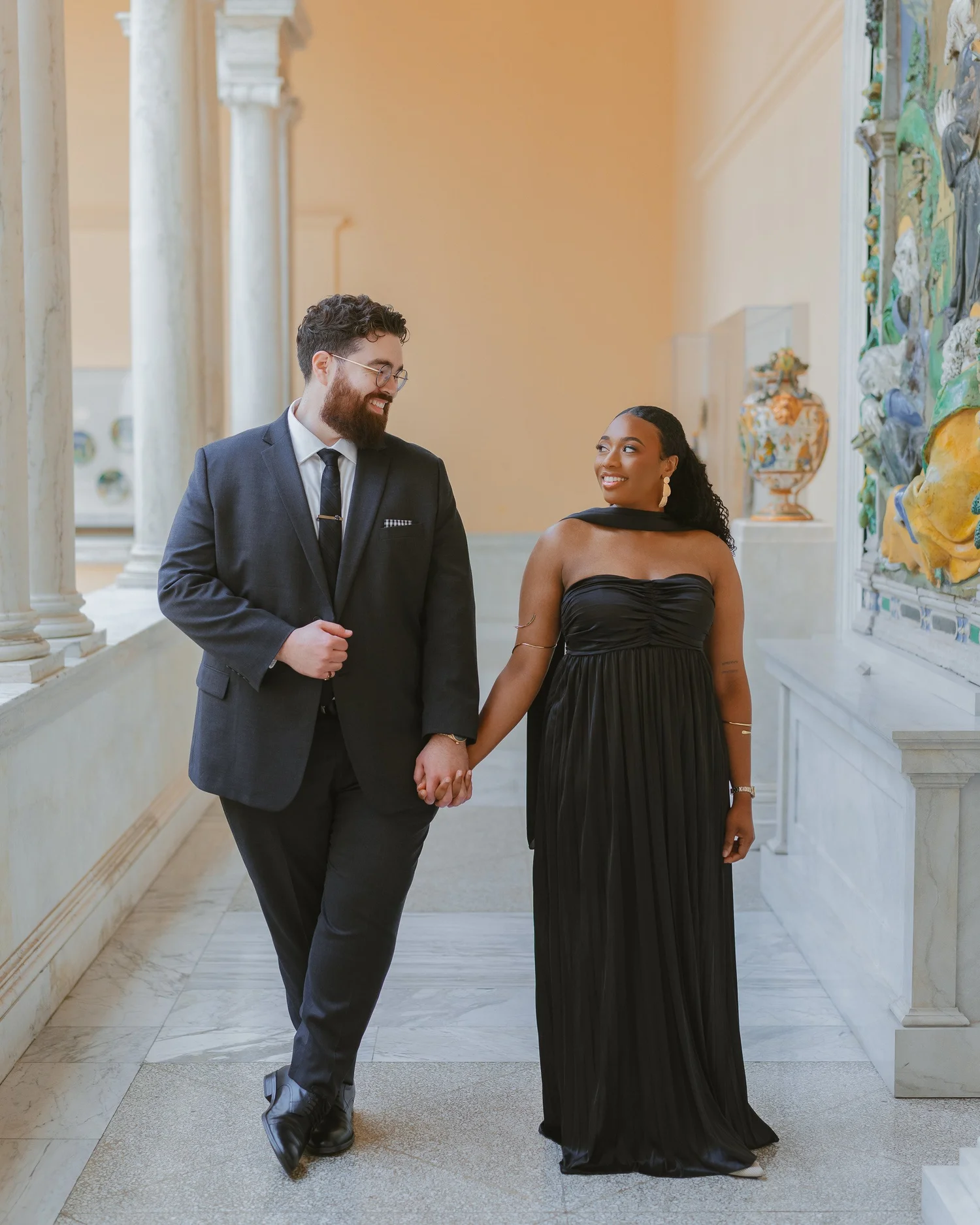 Couple walking hand in hand through a bright museum corridor.