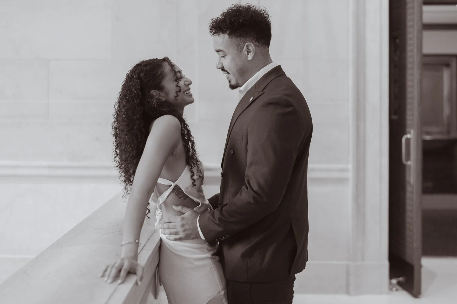 Black-and-white photograph of a couple laughing beside a marble railing.
