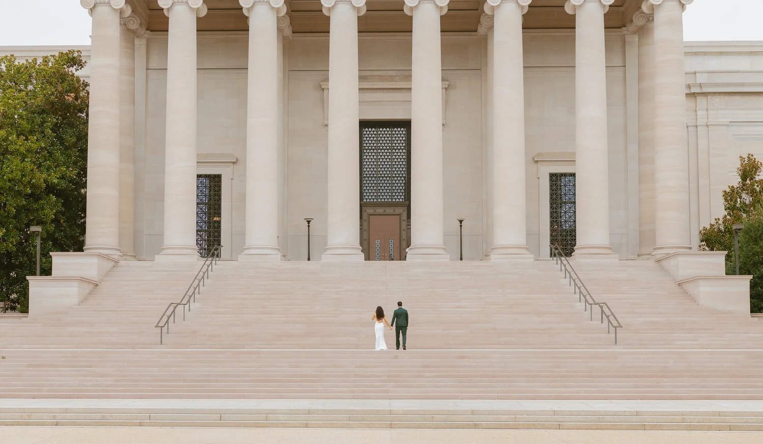 Couple standing hand in hand beneath the National Gallery's tall columns.