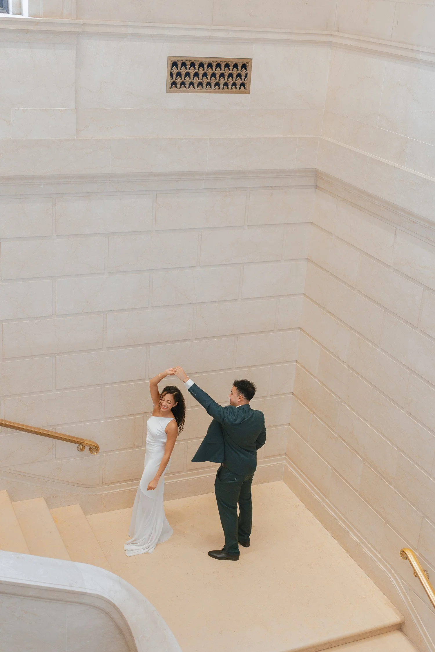Overhead view of a couple turning together on a pale marble stair landing.