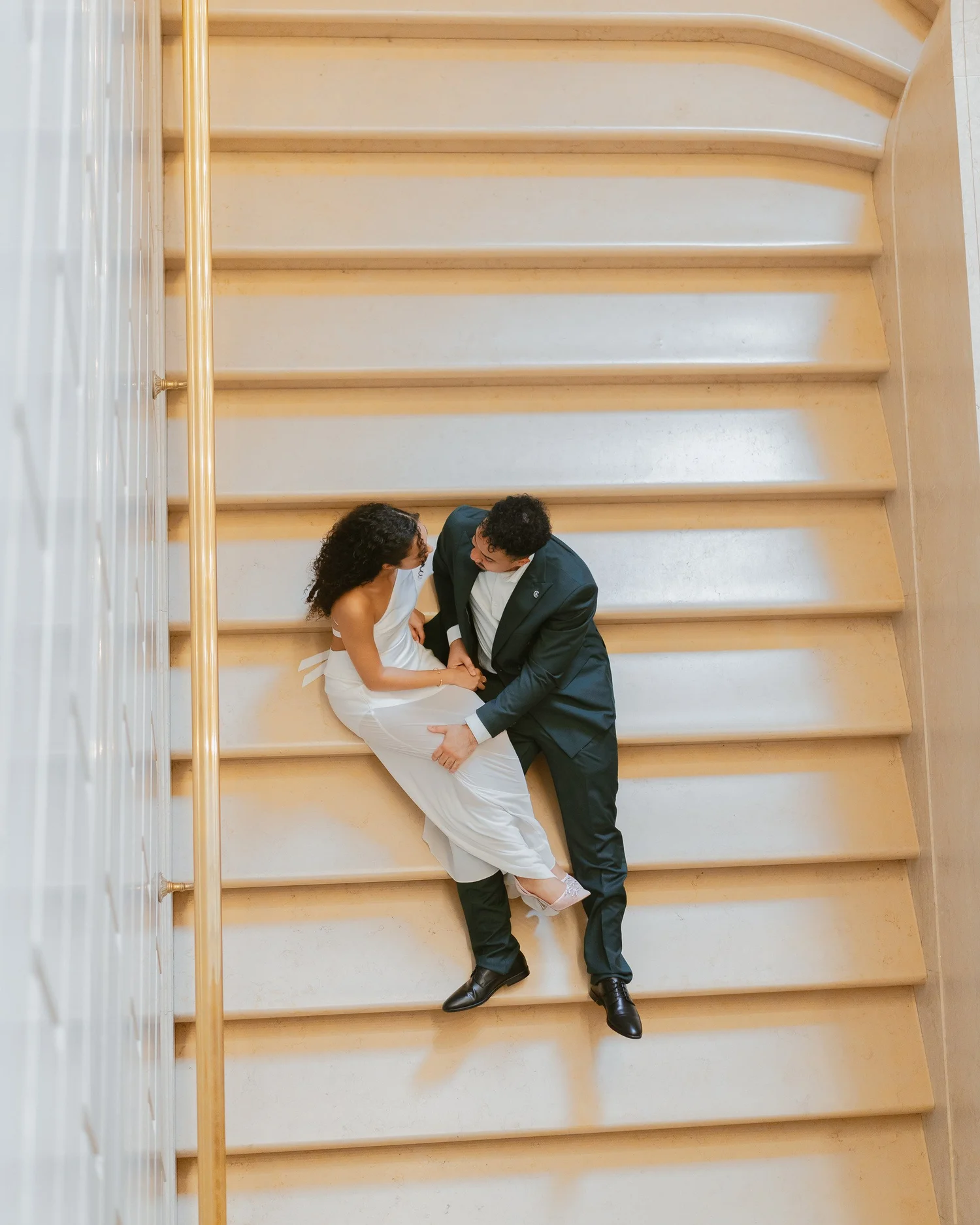 Overhead view of a couple seated together on a pale staircase.