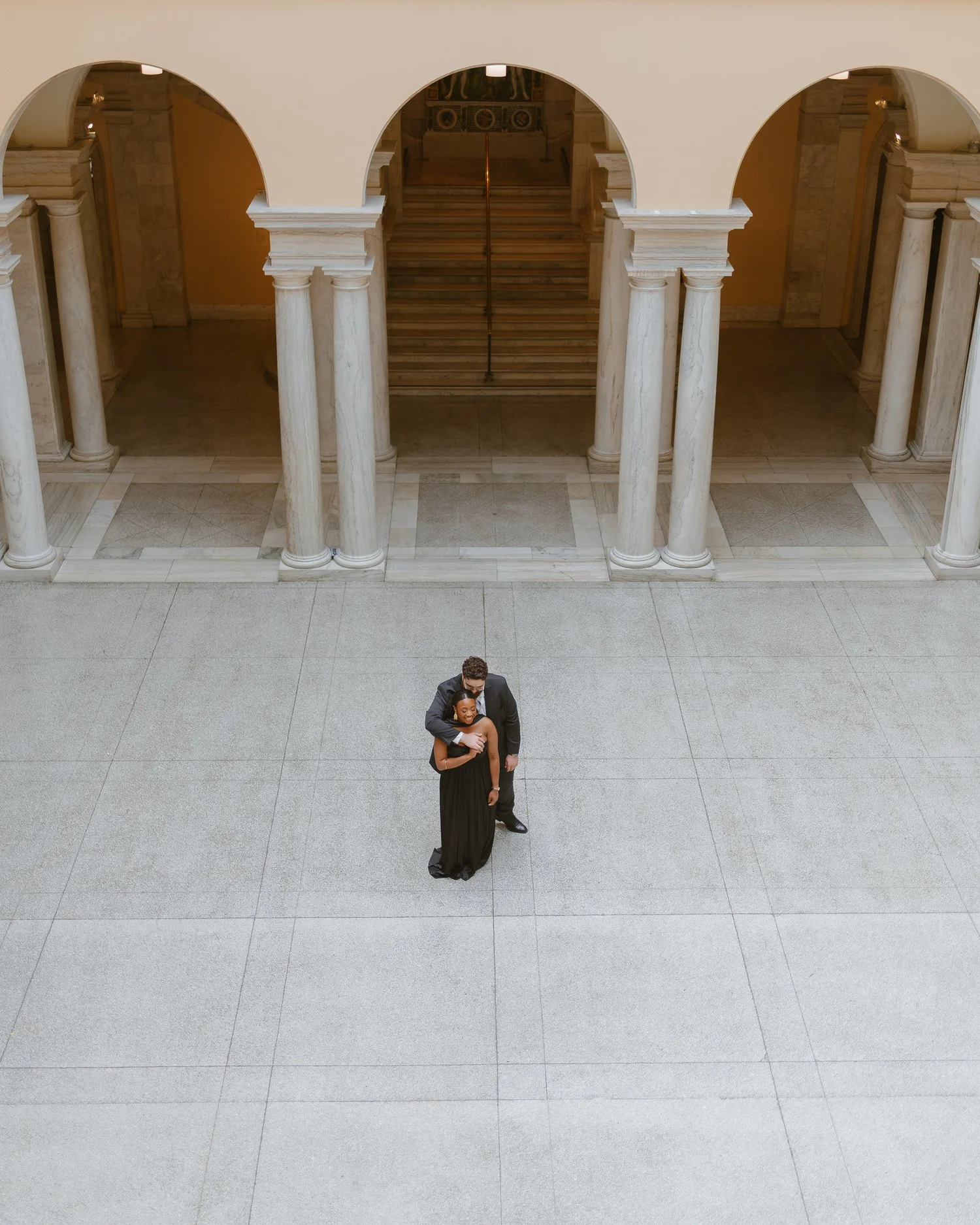 Overhead view of a couple embracing beneath museum arches.