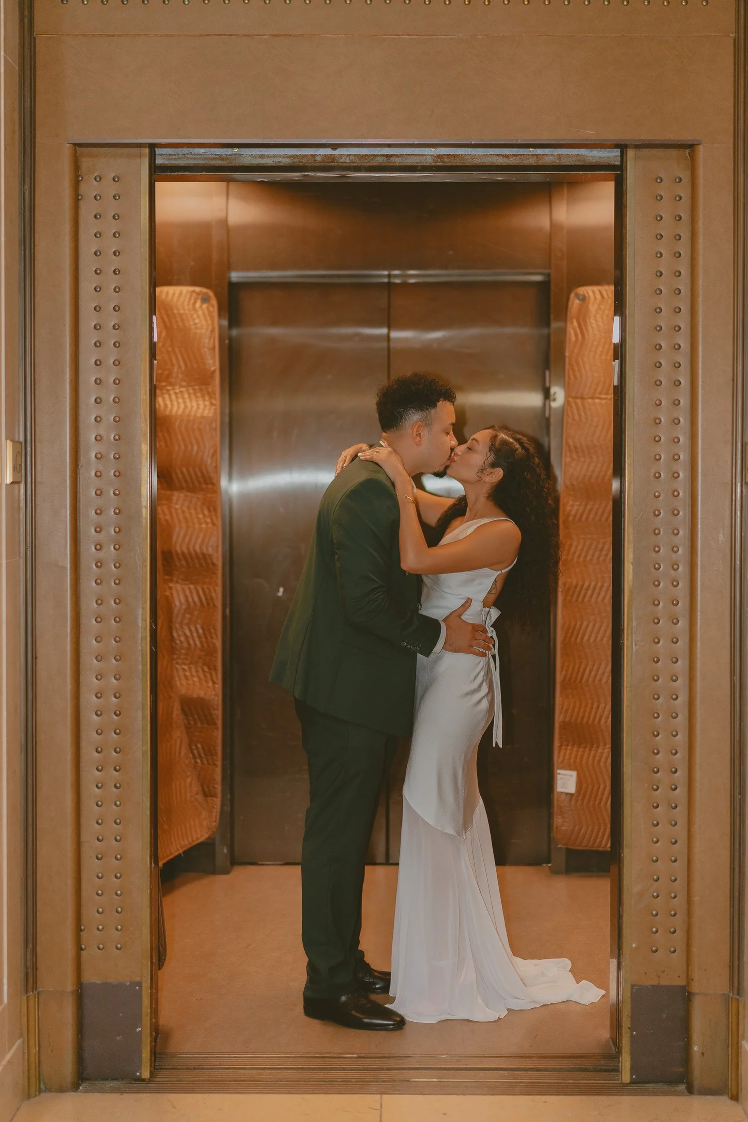 Couple kissing in the doorway of a brass elevator.