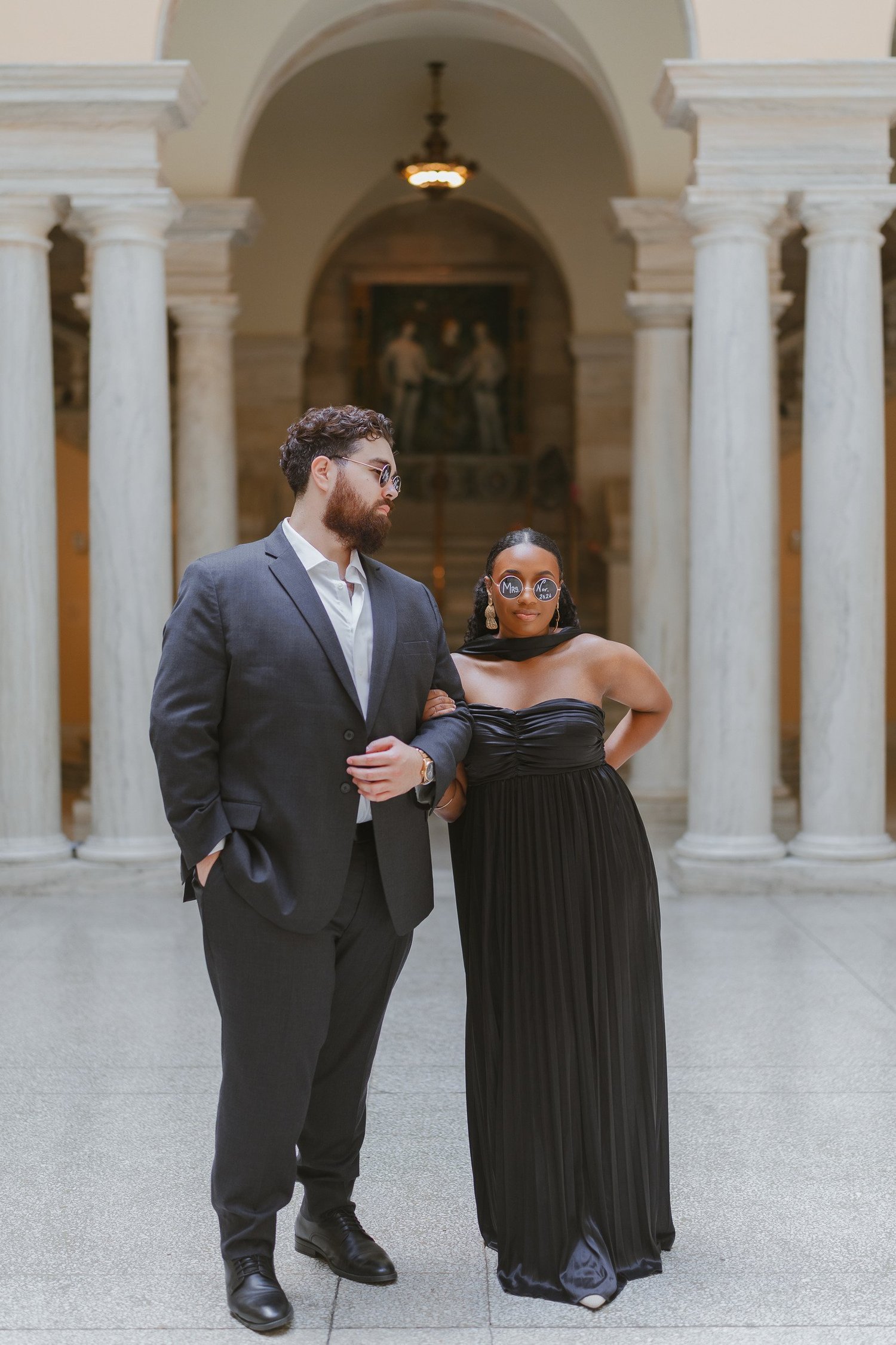 Couple wearing playful sunglasses while standing beneath a museum arch.