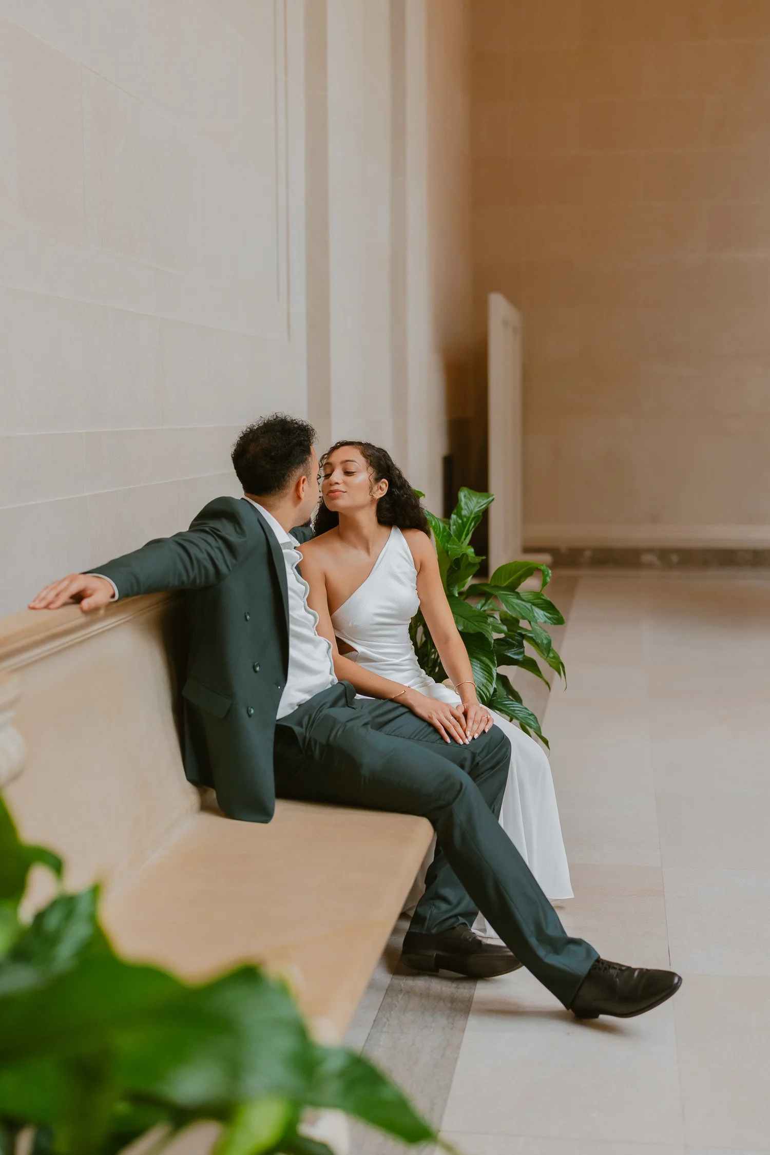 Couple leaning toward a kiss on a stone bench beside greenery.
