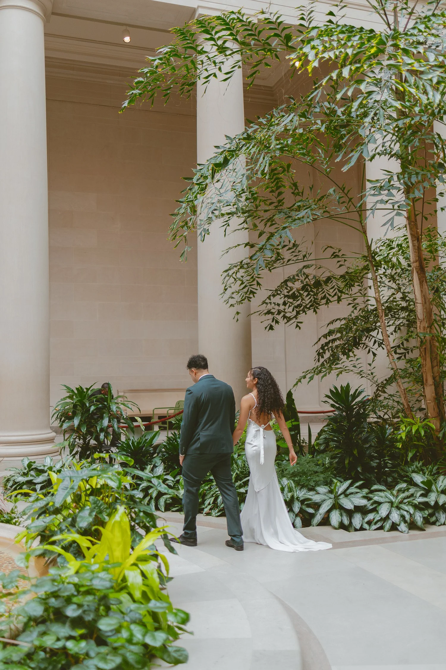 Couple holding hands as they walk through an indoor garden.