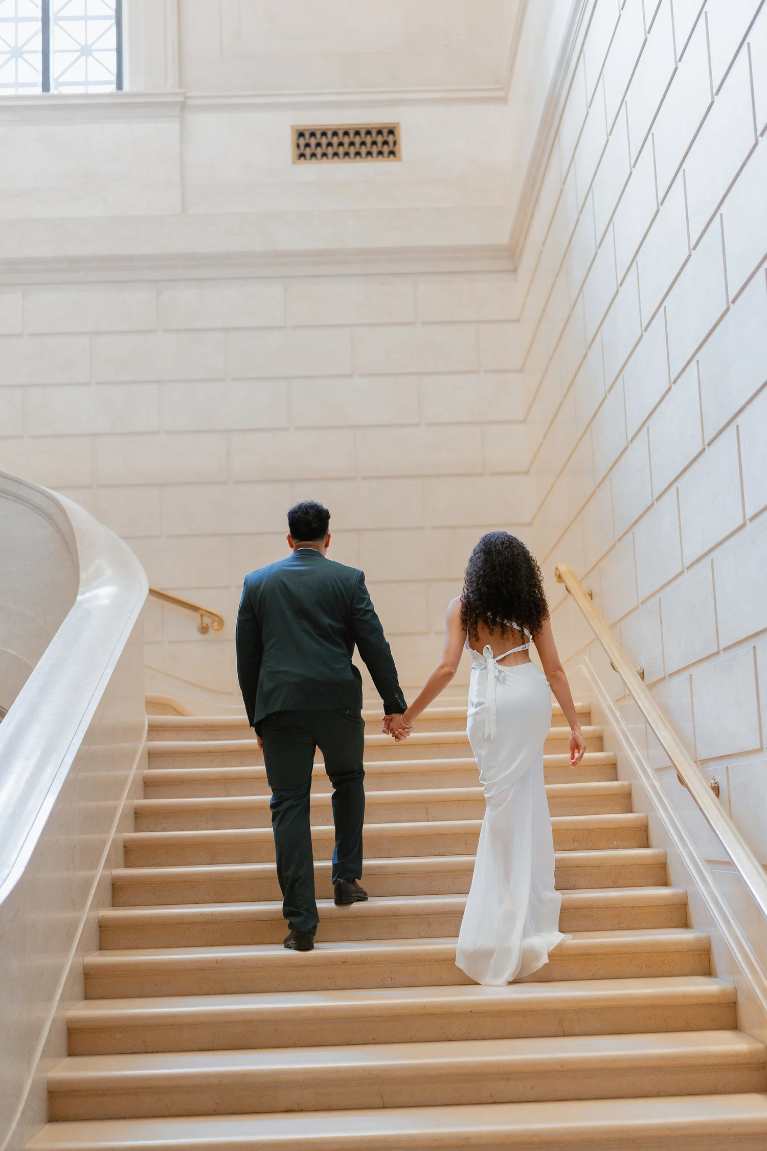 Couple walking hand in hand up a curved marble staircase.