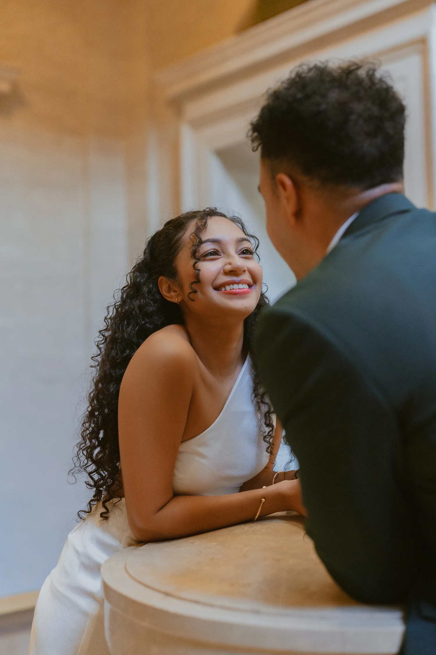 A woman smiling up at her partner beside a marble balustrade.