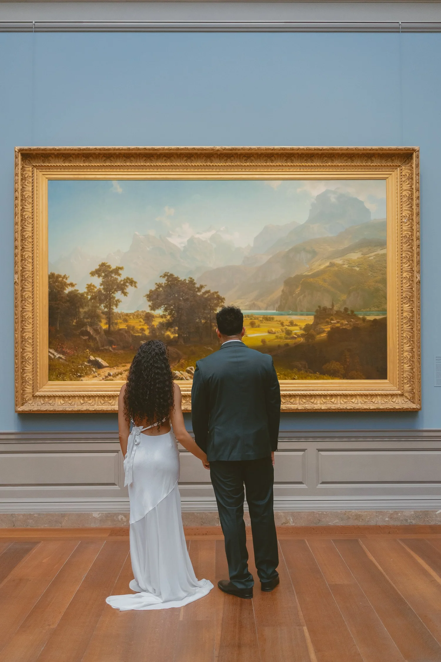 Couple holding hands while looking at a landscape painting.
