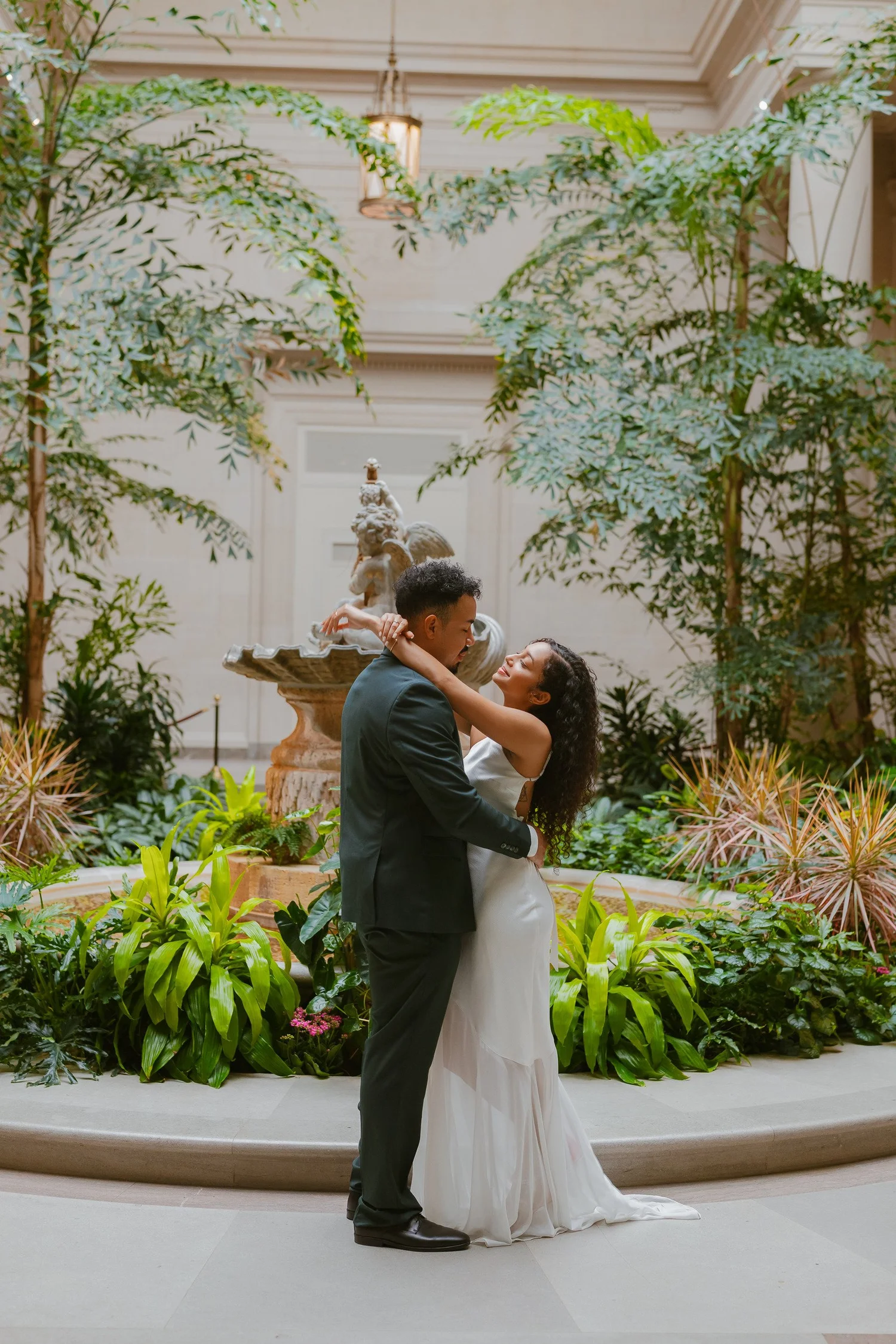 Couple embracing beside a fountain in an indoor garden.