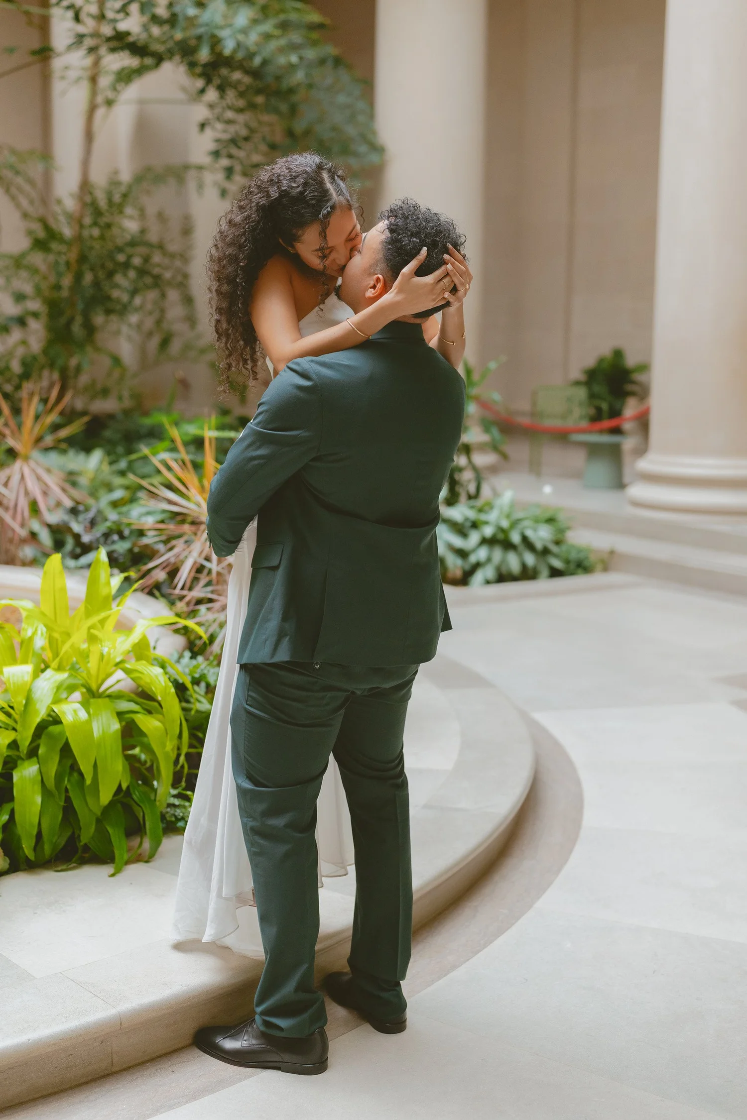 A man lifting his partner in a leafy museum courtyard.