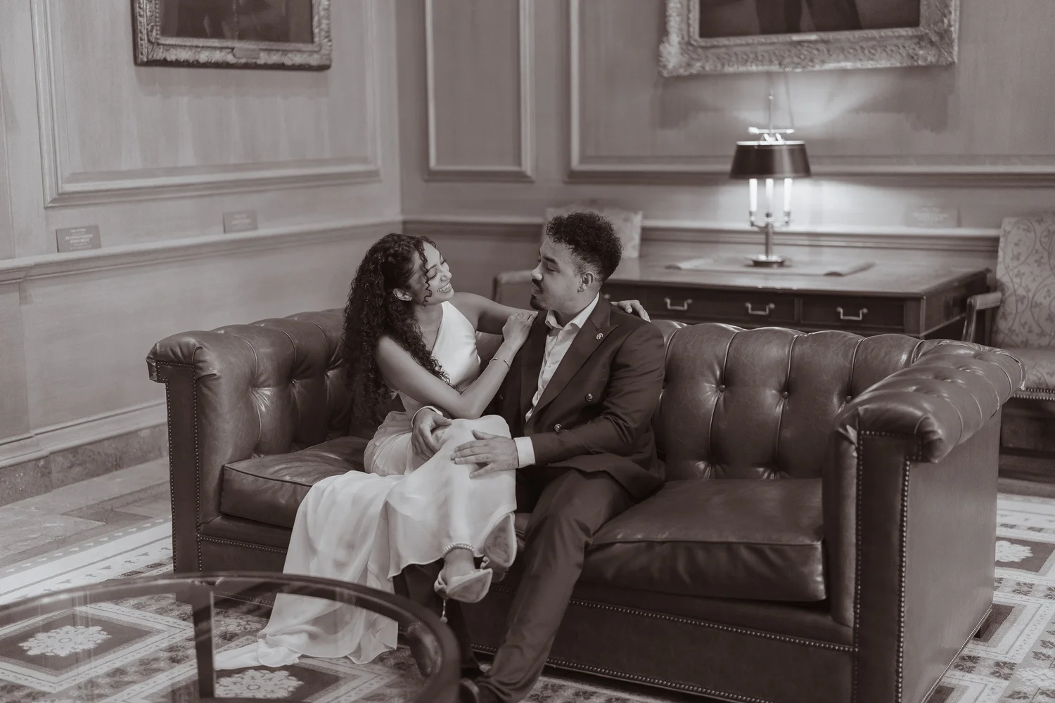 Black-and-white photograph of a couple relaxing together on a leather sofa.