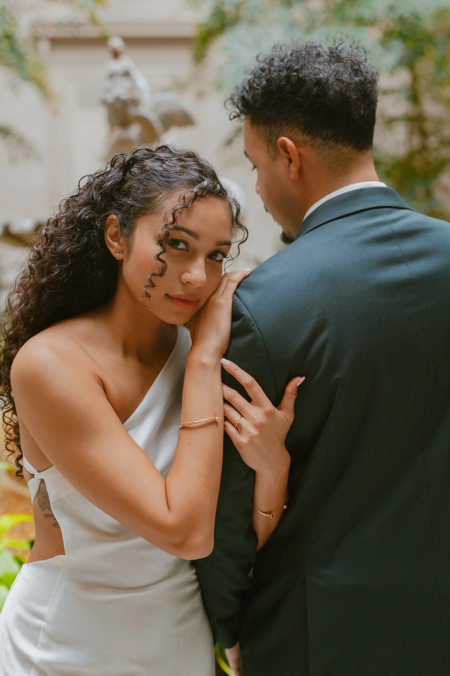 A woman leaning against her partner in a leafy indoor courtyard.