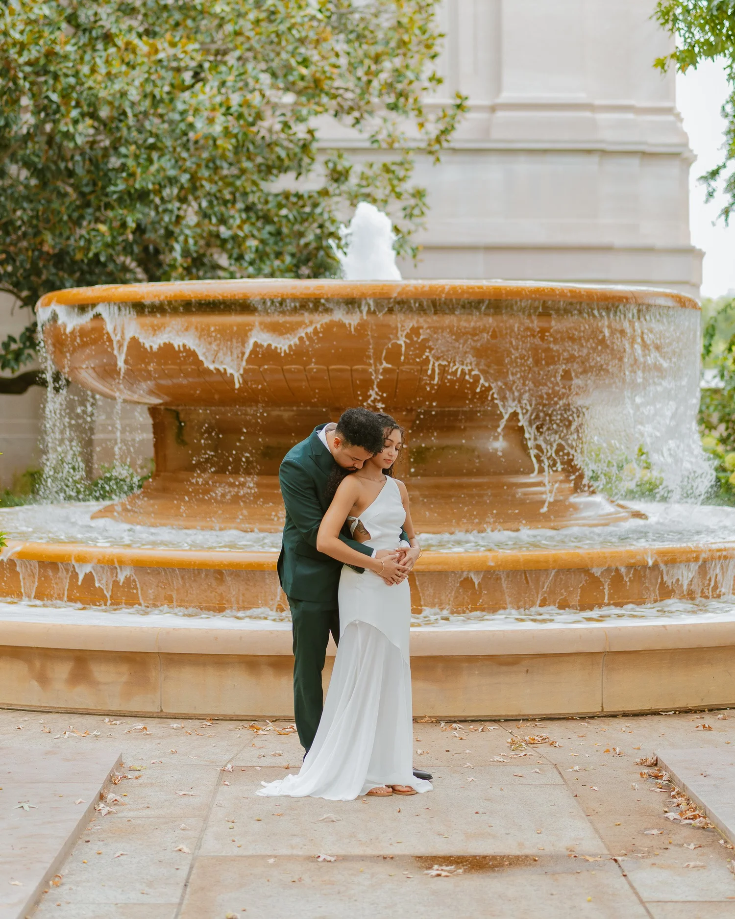 Couple embracing in front of a tiered outdoor fountain.