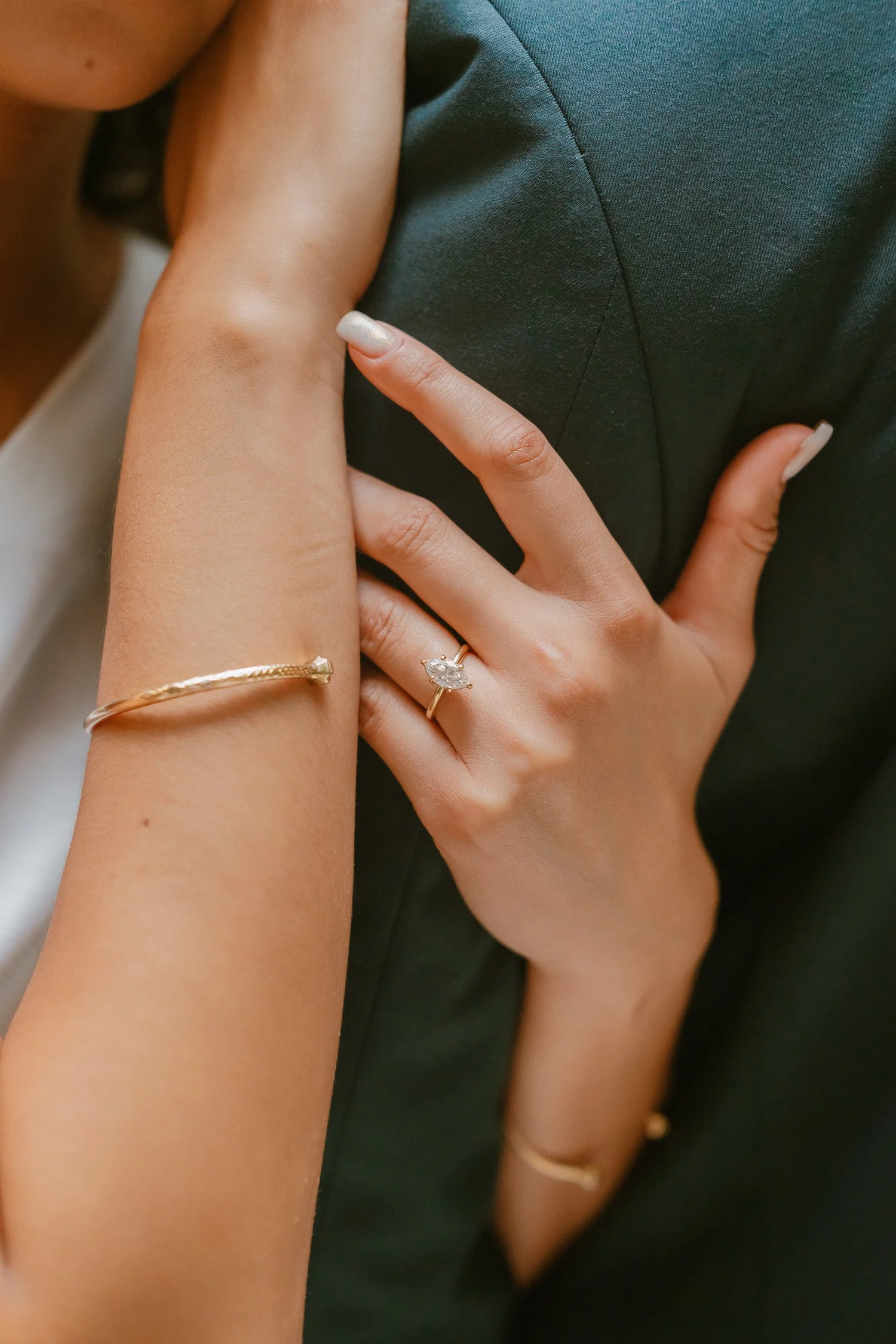 Close-up of an engagement ring as a hand rests on a partner's green jacket.
