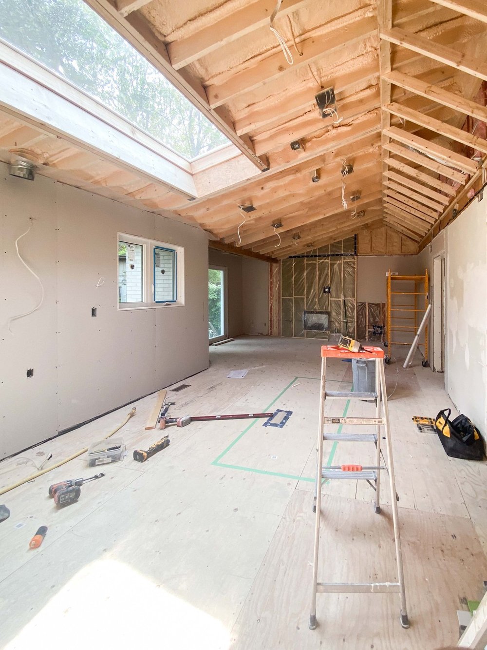 Drywall installation in progress with an open insulated ceiling and skylight
