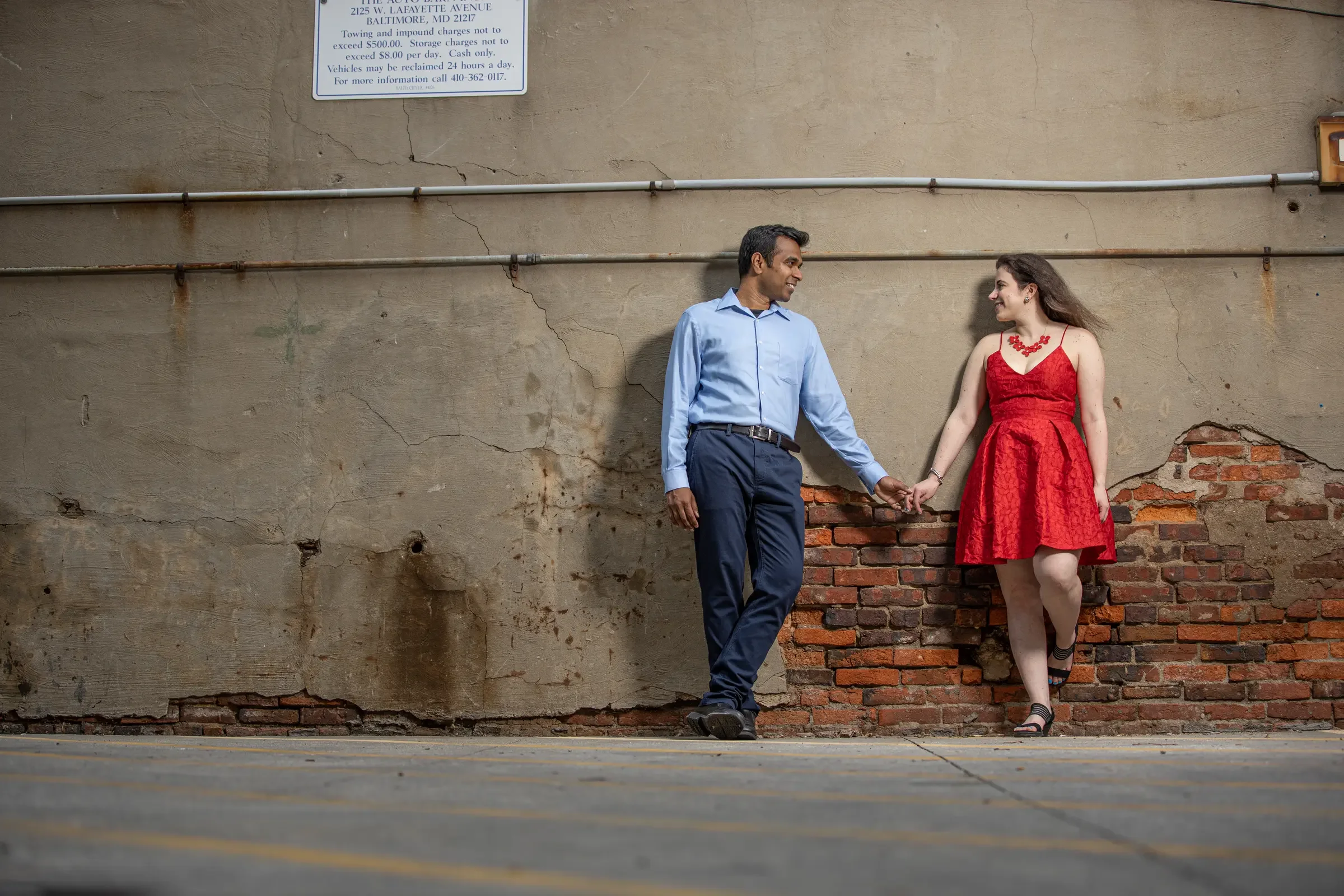 Mallory and Gabe holding hands against a textured Baltimore wall