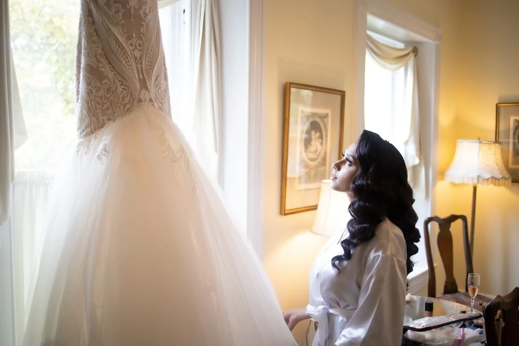 A bride seated beside her wedding gown in soft window light