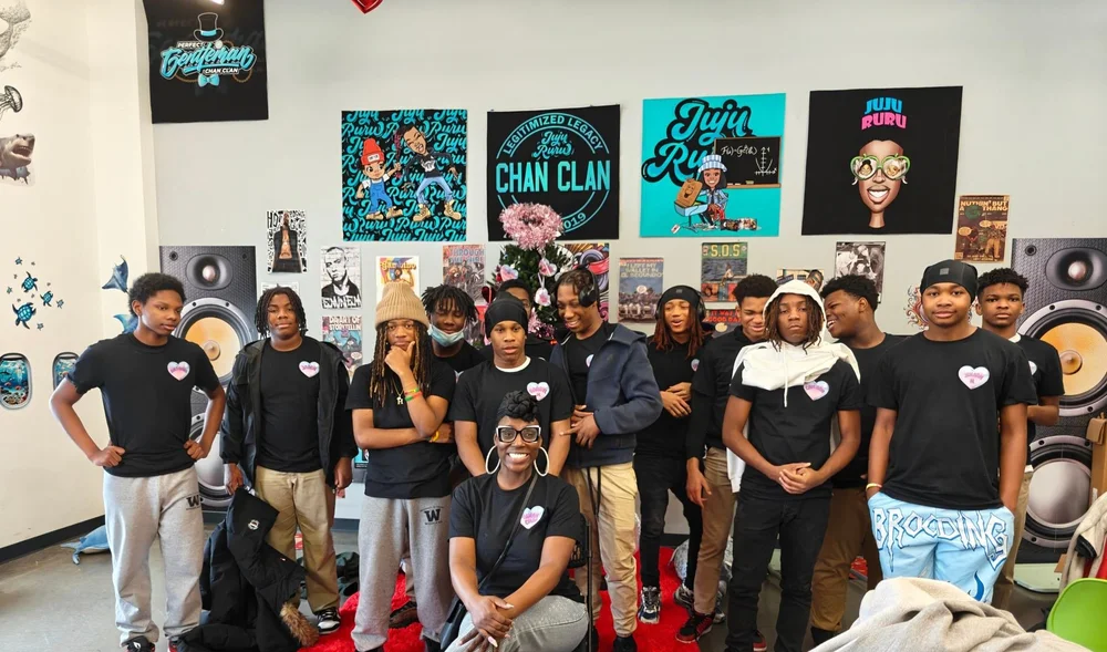 A Chan Clan cohort of teens in front of a studio wall of Chan Clan artwork and speakers