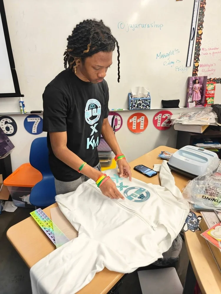 A student lines up his own design on a white hoodie beside a heat press