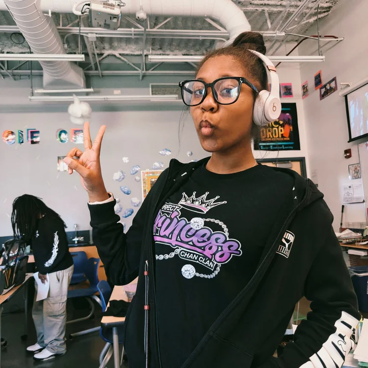 A student in headphones and a Chan Clan Perfect Princess hoodie throws up a peace sign