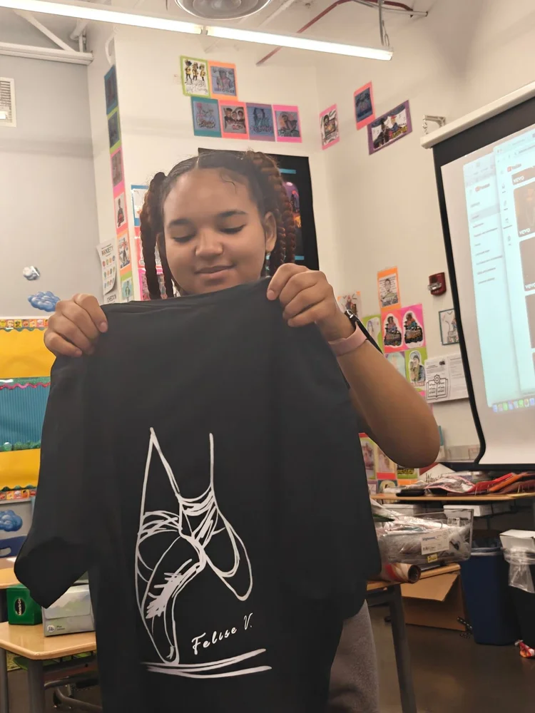A student holds up a black t-shirt with her own ballet-shoe illustration and signature