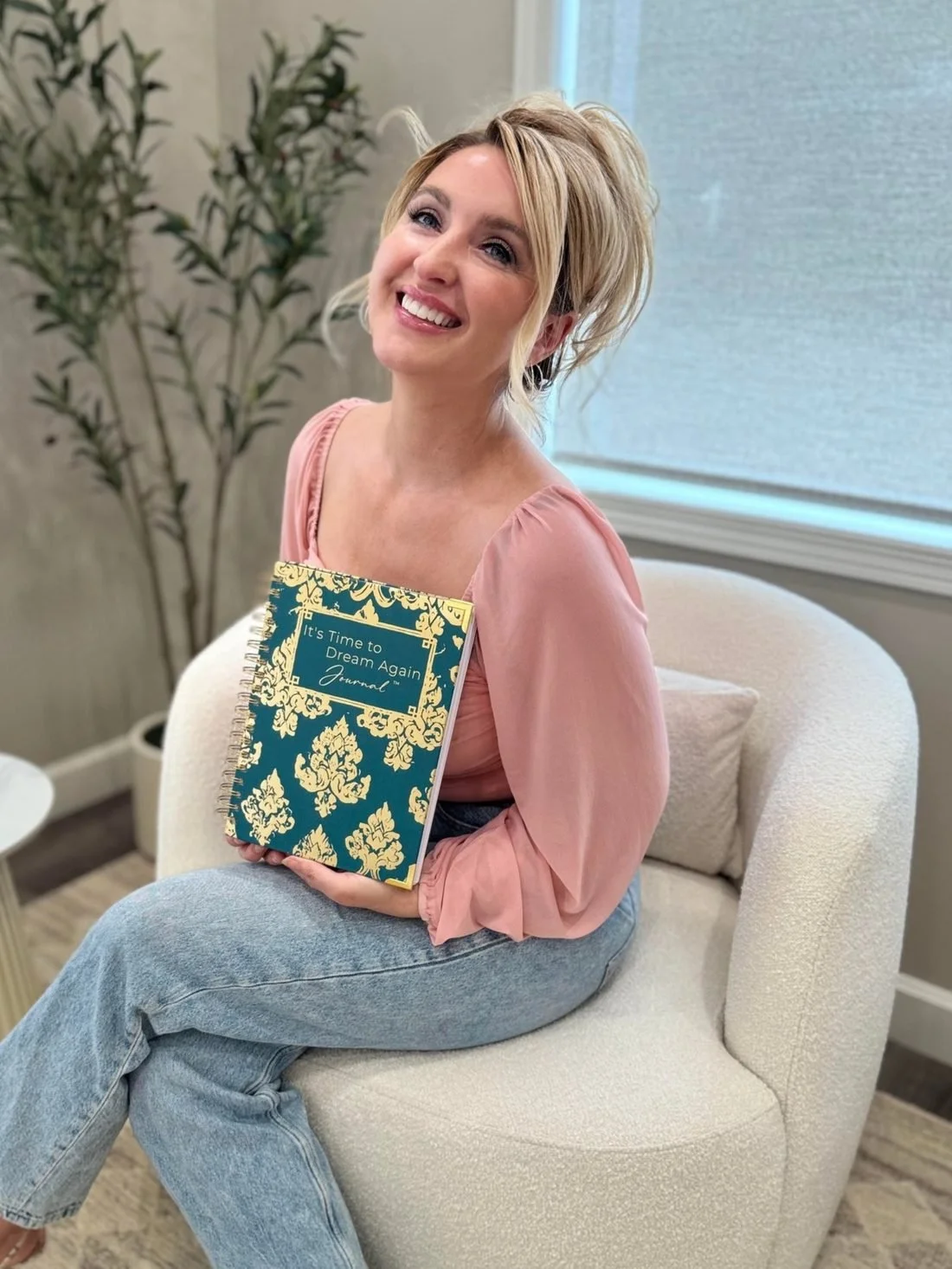 Dawn Towne smiling in a cream chair, holding the It's Time to Dream Again journal