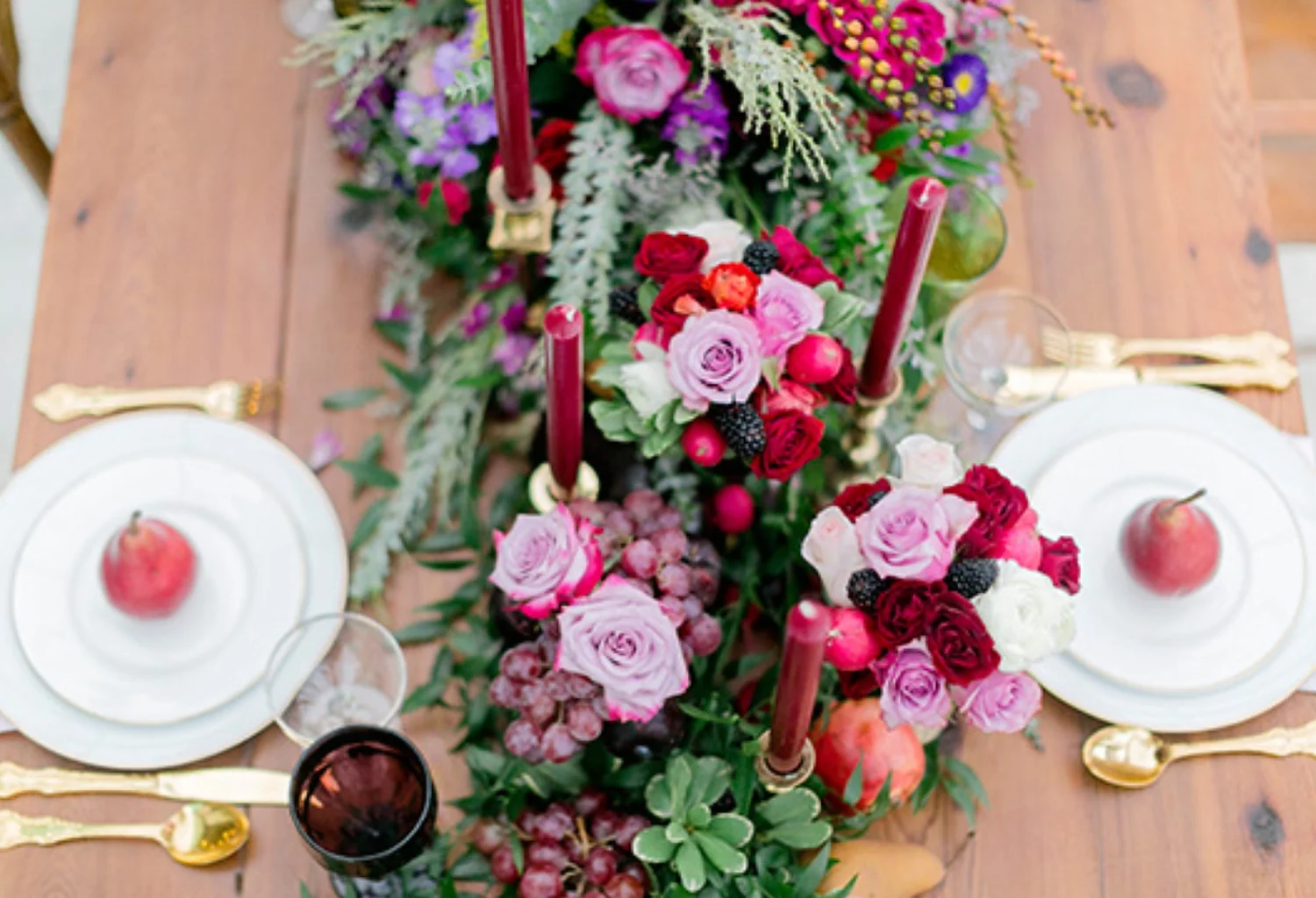Overhead view of a farm table with a garden-rose, grape and berry runner, burgundy tapers, gold flatware and pear place settings