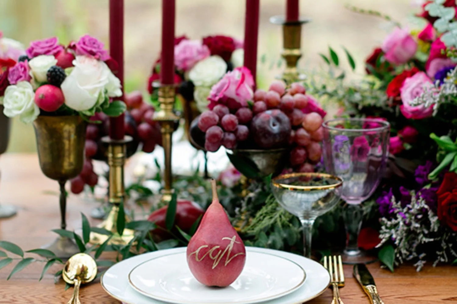 A jewel-toned tablescape with burgundy tapers, roses, grapes and a gold-lettered pear place card