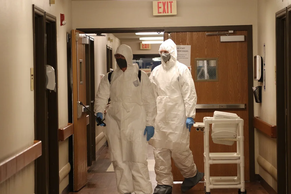 Workers in protective suits and respirators disinfecting a building hallway