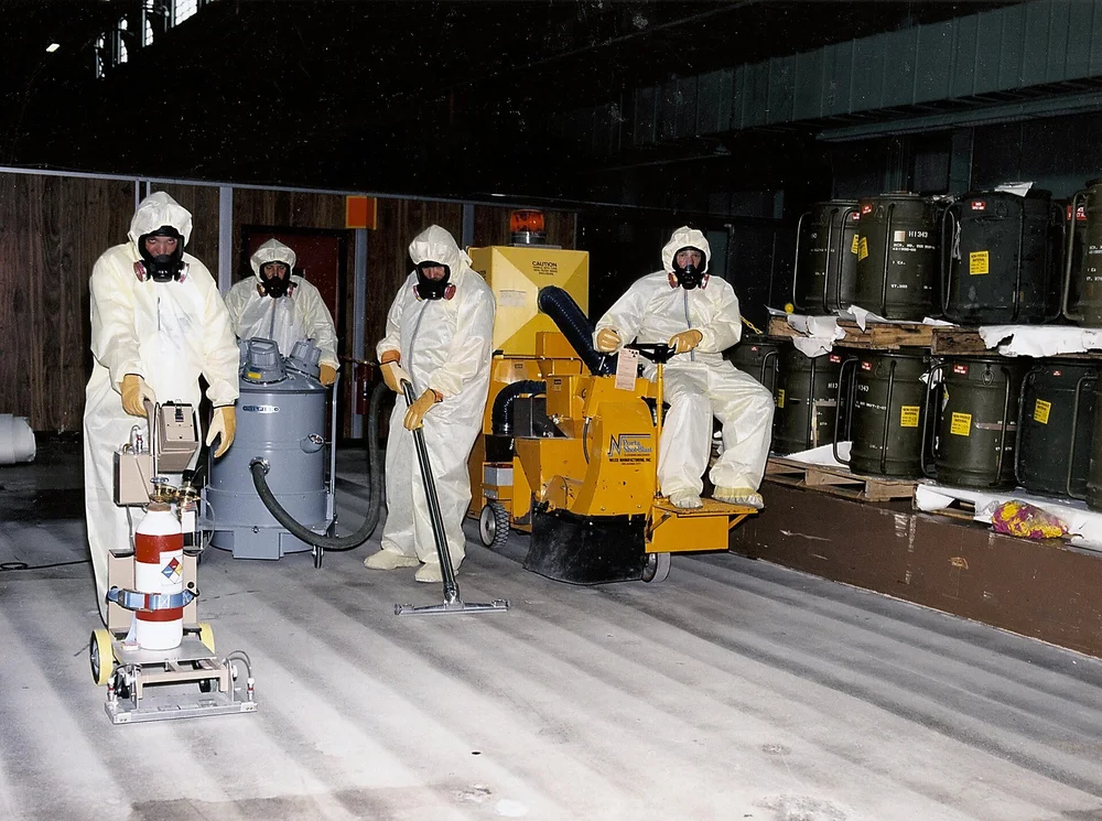Workers in protective suits cleaning a floor inside a large facility