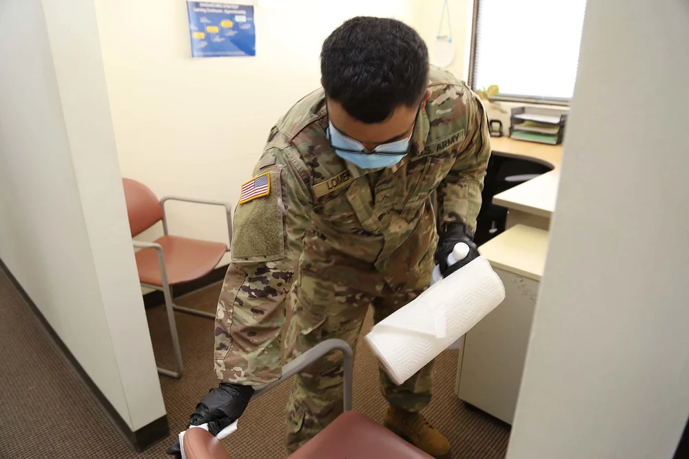 Masked worker wearing gloves wiping down a desk surface