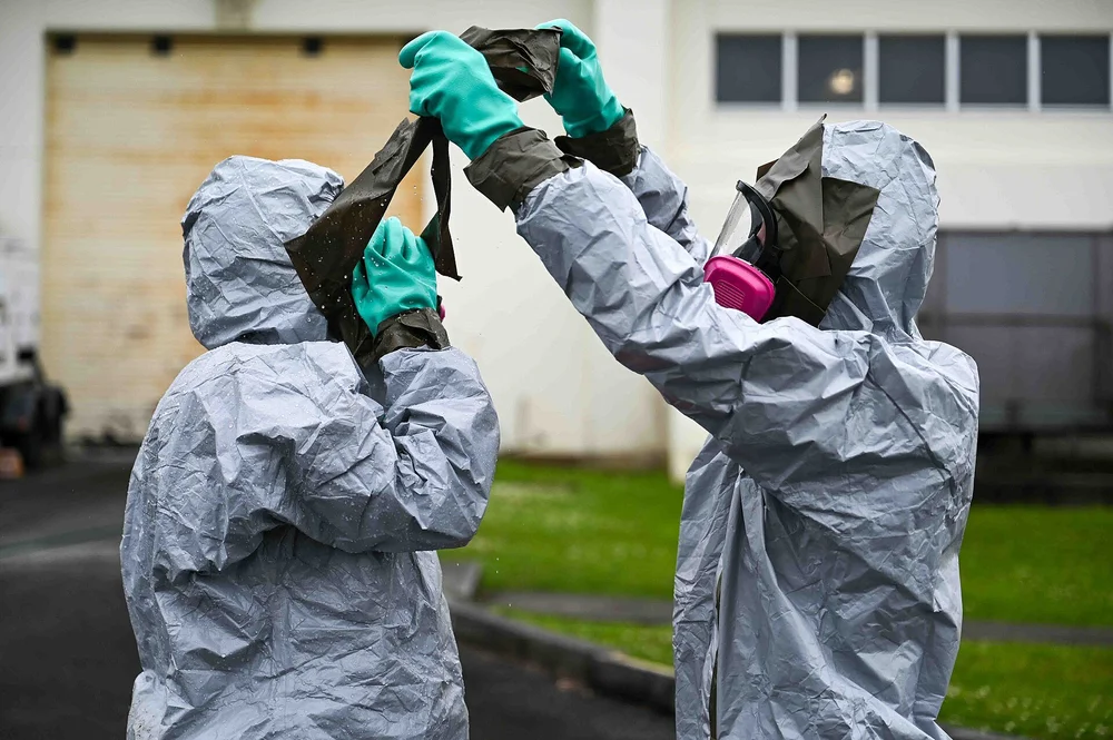 Two workers in protective suits and respirators helping each other with gloves