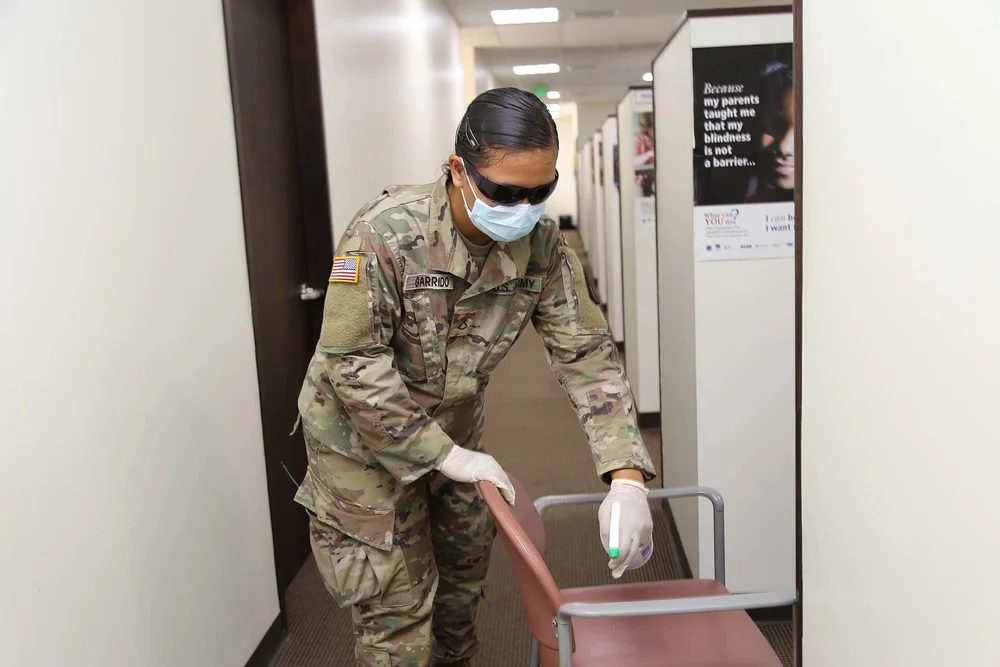 Worker in gloves and mask pushing a cleaning cart down a hallway