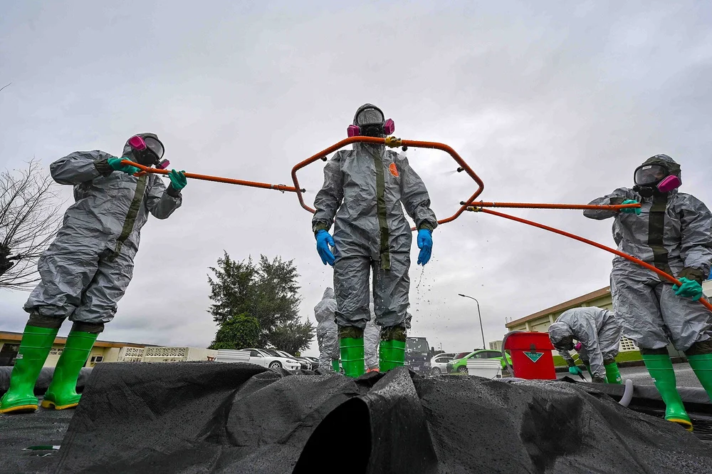 Team members in gray protective suits rinsing a colleague at a decontamination training station